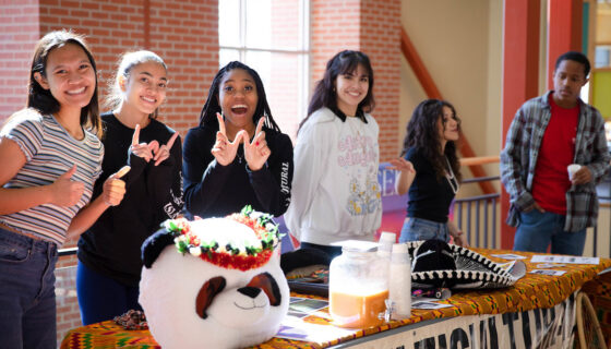A few students pose for a photo behind the Multicultural Center table at the Admitted Student Day Club Fair.