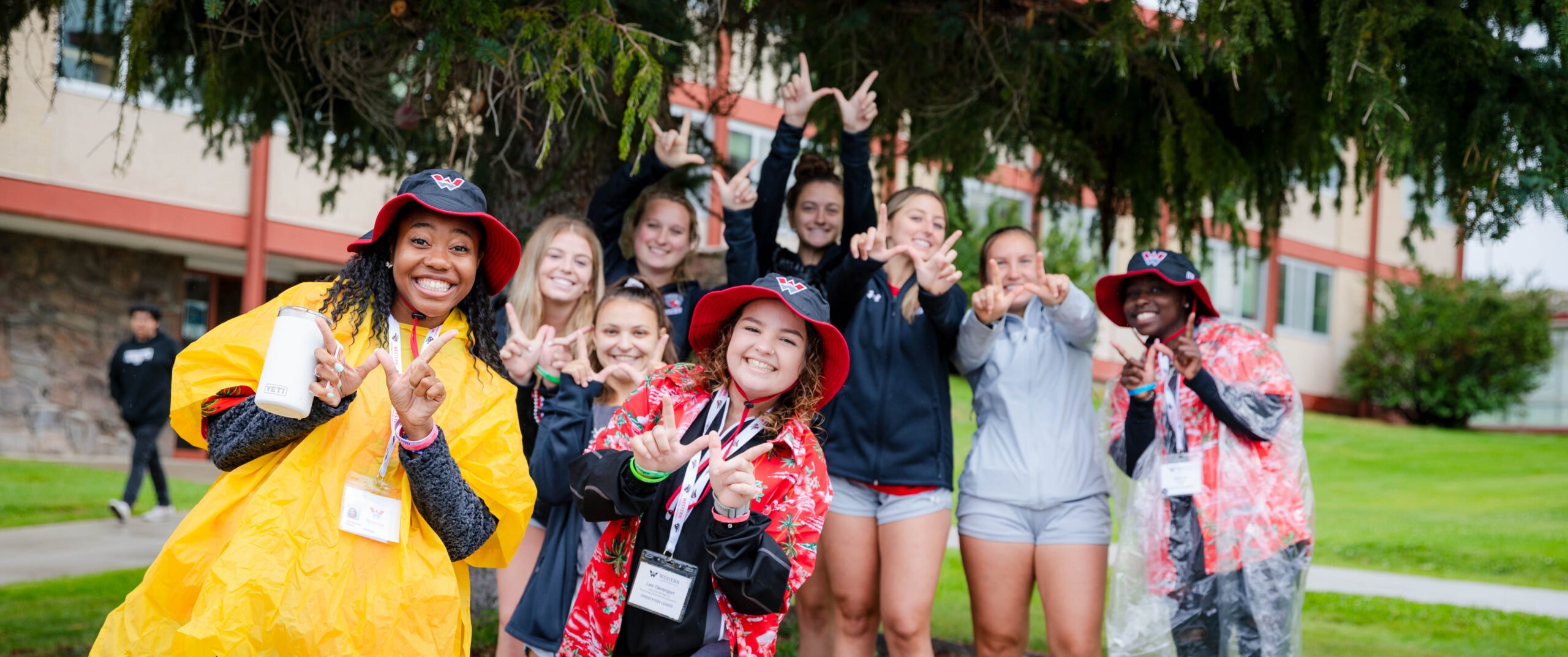 Orientation leaders and members of the women's soccer team gather for a group photo with their hands giving the W symbol in front of the Escalante Complex