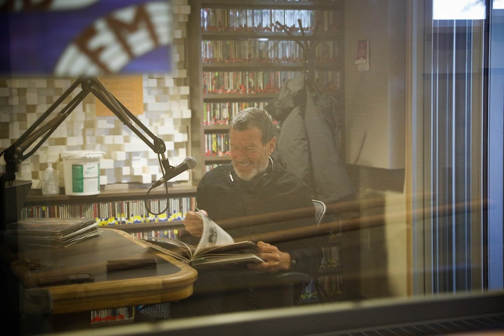 A photo through the window of the KWSB studio of alum Michael Johnson looking through an old KWSB photo book.