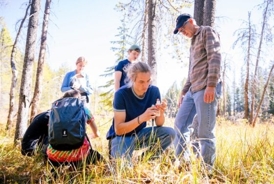 A student kneels on grass and injects acid into a water sample as his class watches.