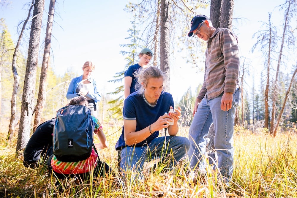 A student kneels on grass and injects acid into a water sample as his class watches.