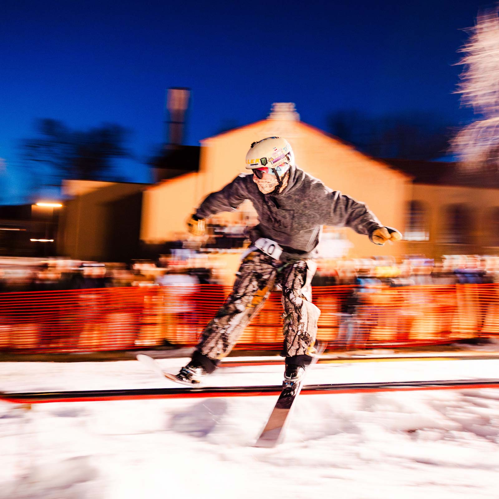 A skier slides a rail in front of the library while students cheer for him in the background. A motion blur effect is used in this photo.