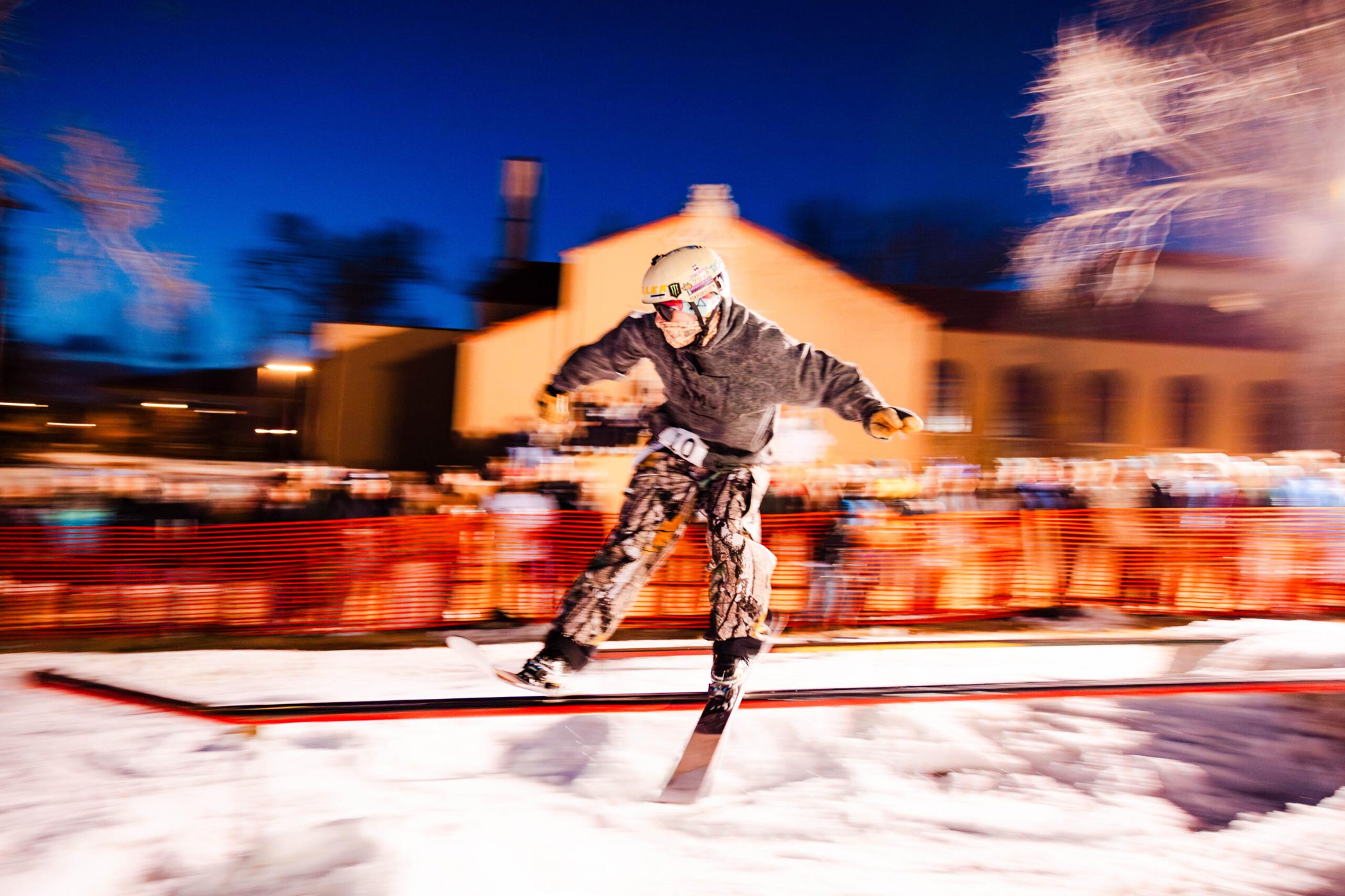 A skier slides a rail in front of the library while students cheer for him in the background. A motion blur effect is used in this photo.