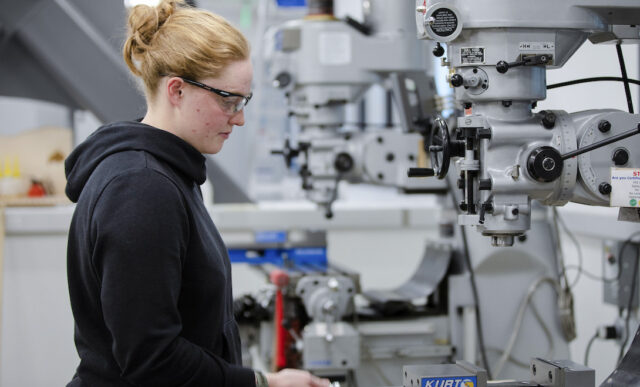 Engineering student, Carolyn Goodwin, wears safety glasses and uses a machine in one of the shops in the Rady Building.