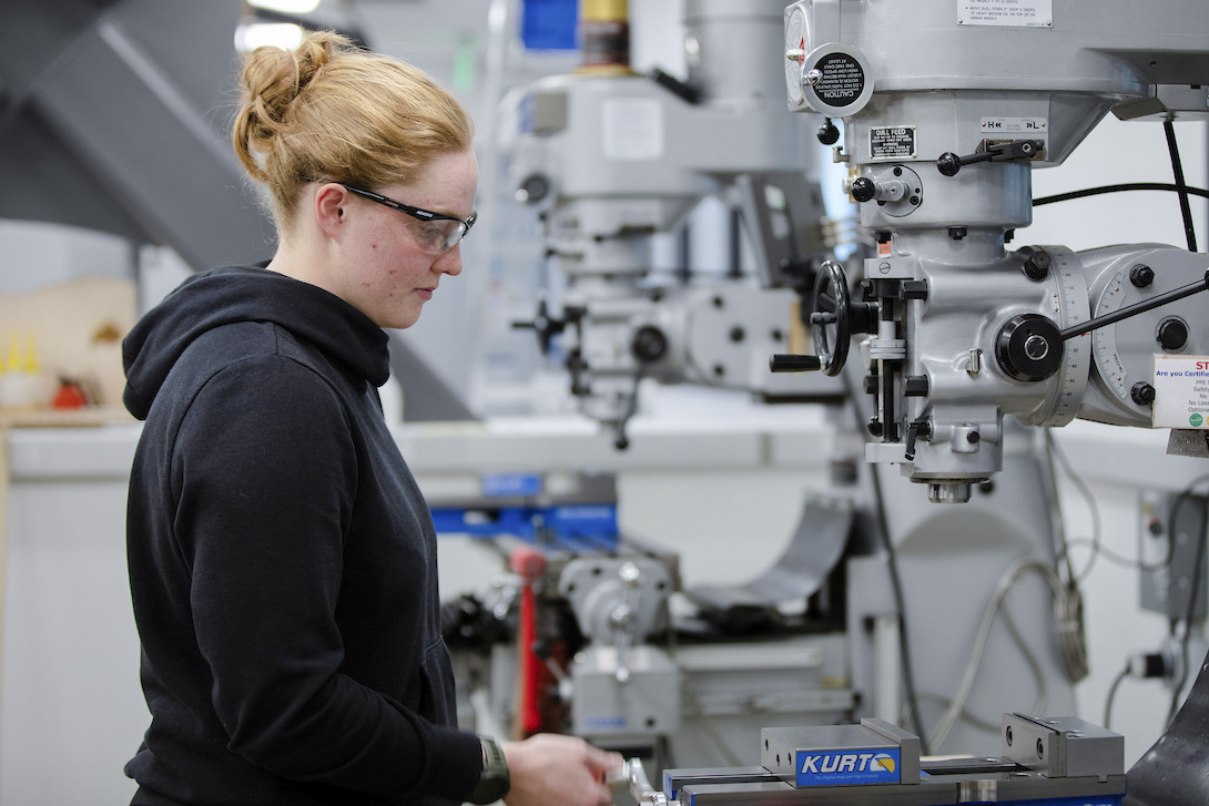 Engineering student, Carolyn Goodwin, wears safety glasses and uses a machine in one of the shops in the Rady Building.