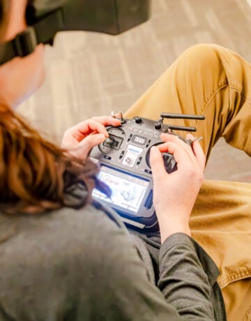 A student sits while wearing a headset as he flies a drone using a controller.