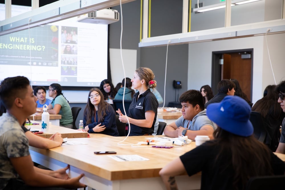 Lauren Cooper walks around a classroom and talks with high school students during and exercise about engineering.