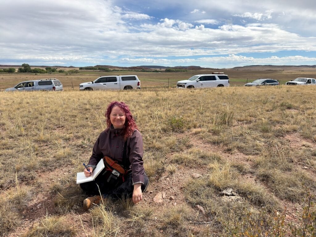 Erica Reid sits in a field holding her notebook while on a watershed tour.