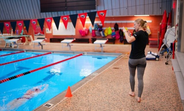 Graduate student, Emily Jauch, with the HAEP program walks the length of the pool as she films a swimmer completing a lap.