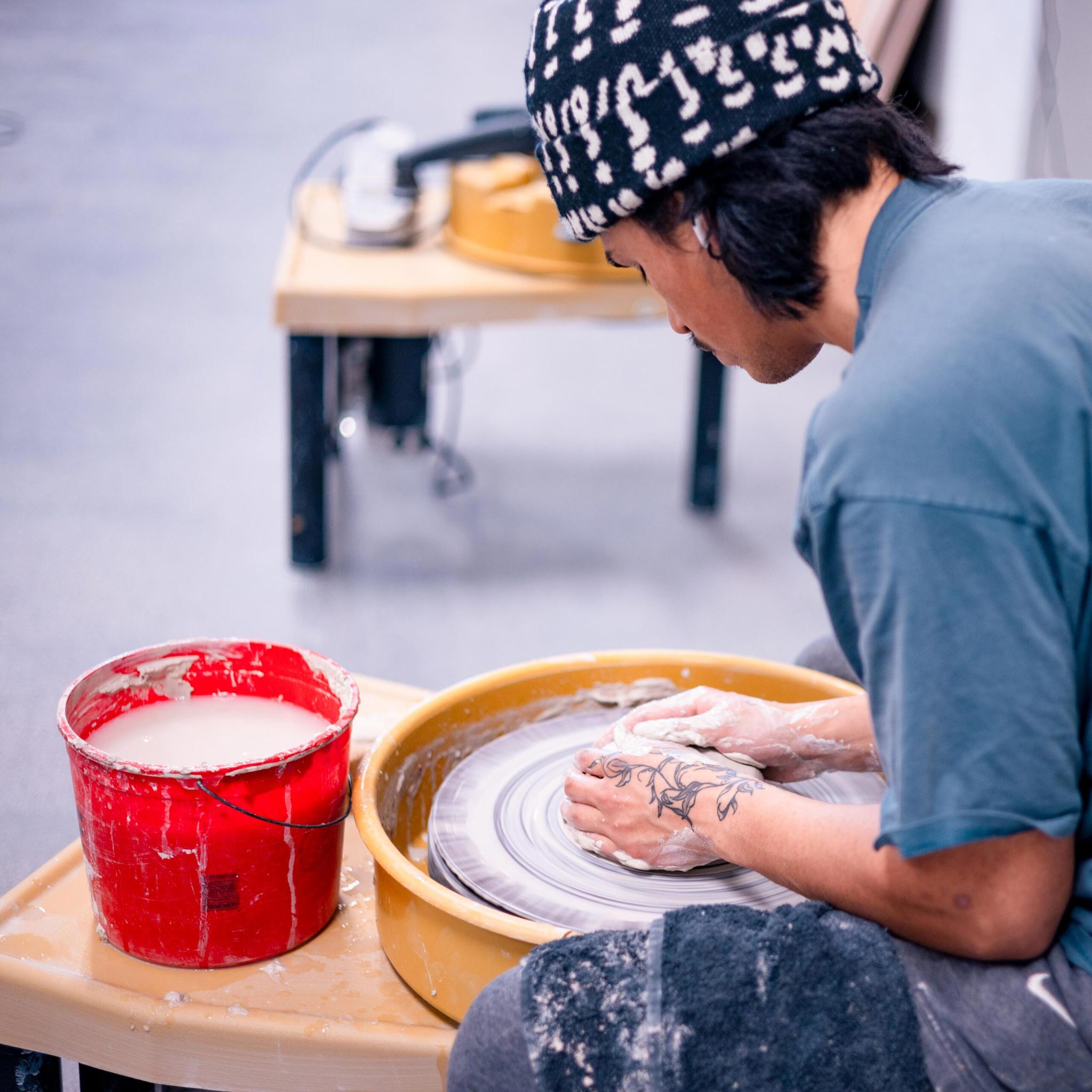 A student is seated at a potter's wheel and starts forming a pot with clay.