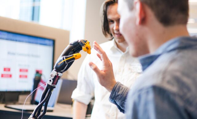 A student holds his hand up against a robotic hand he engineered.