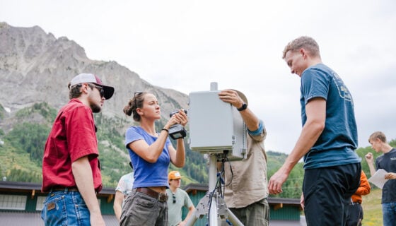 Engineering students and two RMBL employees build a weather station together in Gothic, Colorado with big mountain views behind them.