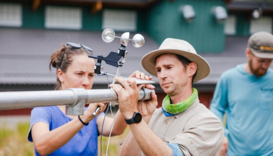 Two RMBL employees install a weather station in front of the RMBL research center.