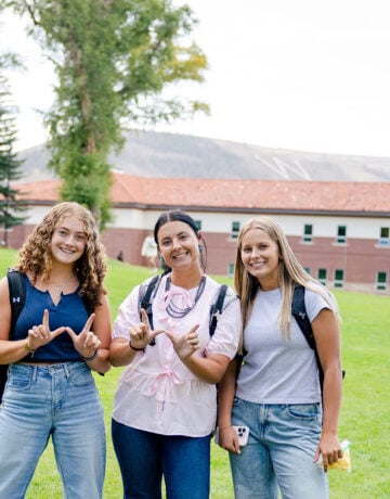 Three girls hold up w's with their hands as they stand on Taylor Lawn.