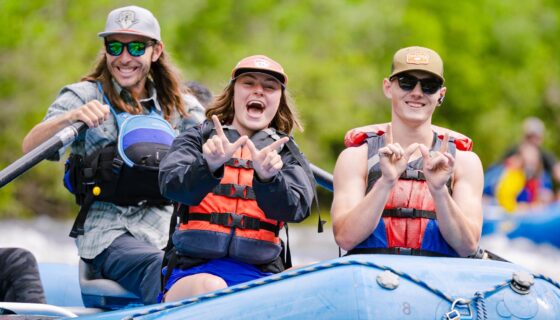 Students wearing life jackets hold up Ws while rafting down the Taylor River.