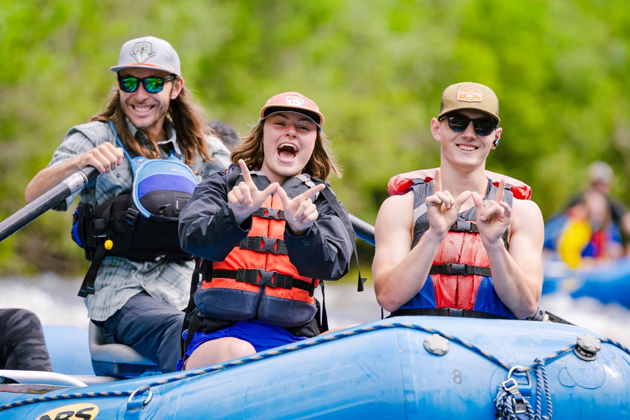 Students wearing life jackets hold up Ws while rafting down the Taylor River.