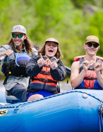 Students wearing life jackets hold up Ws while rafting down the Taylor River.