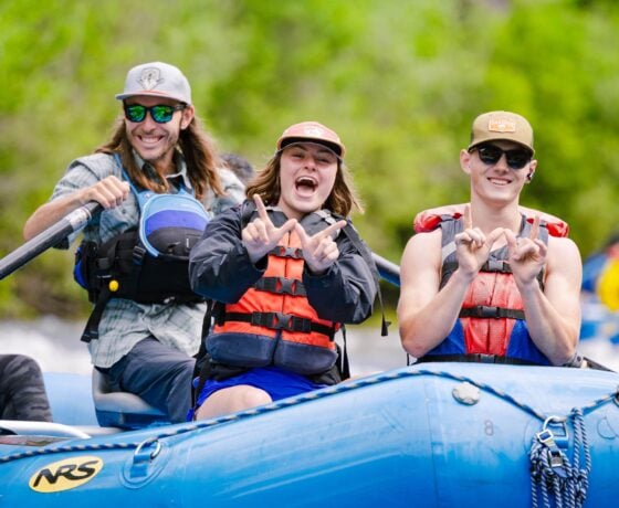 Students wearing life jackets hold up Ws while rafting down the Taylor River.