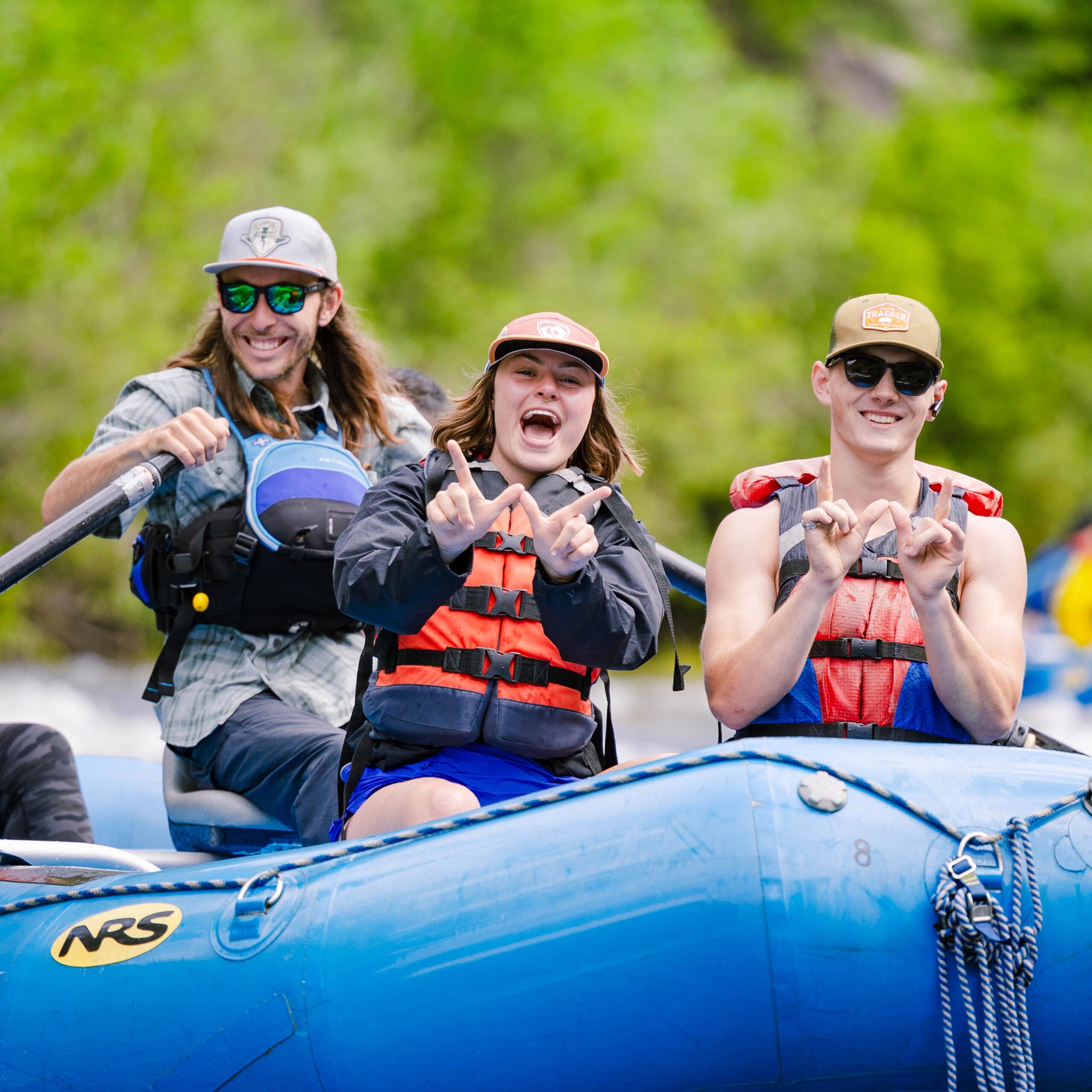 Students wearing life jackets hold up Ws while rafting down the Taylor River.