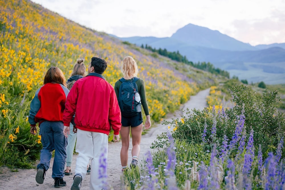 A group of friends walk down the Brush Creek Trail surrounded by wildflowers during the sunrise.