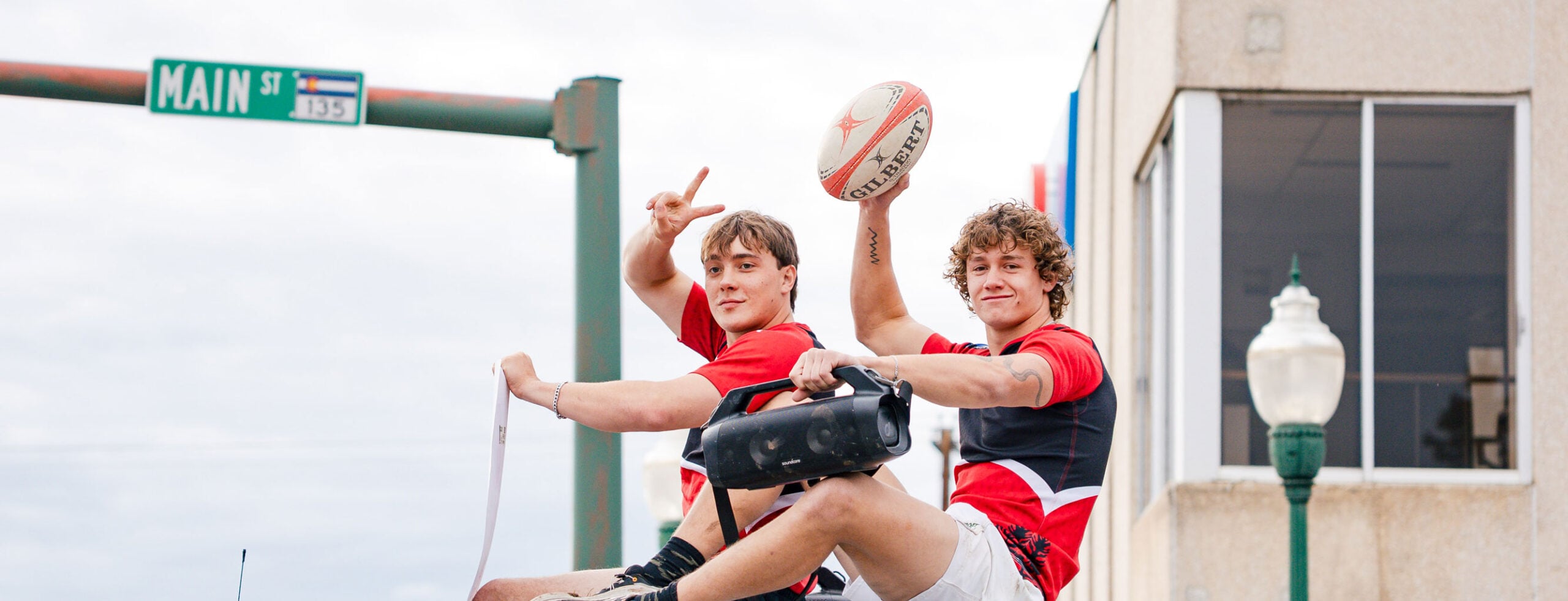 Two rugby players sit on top of a truck during the Homecoming parade.