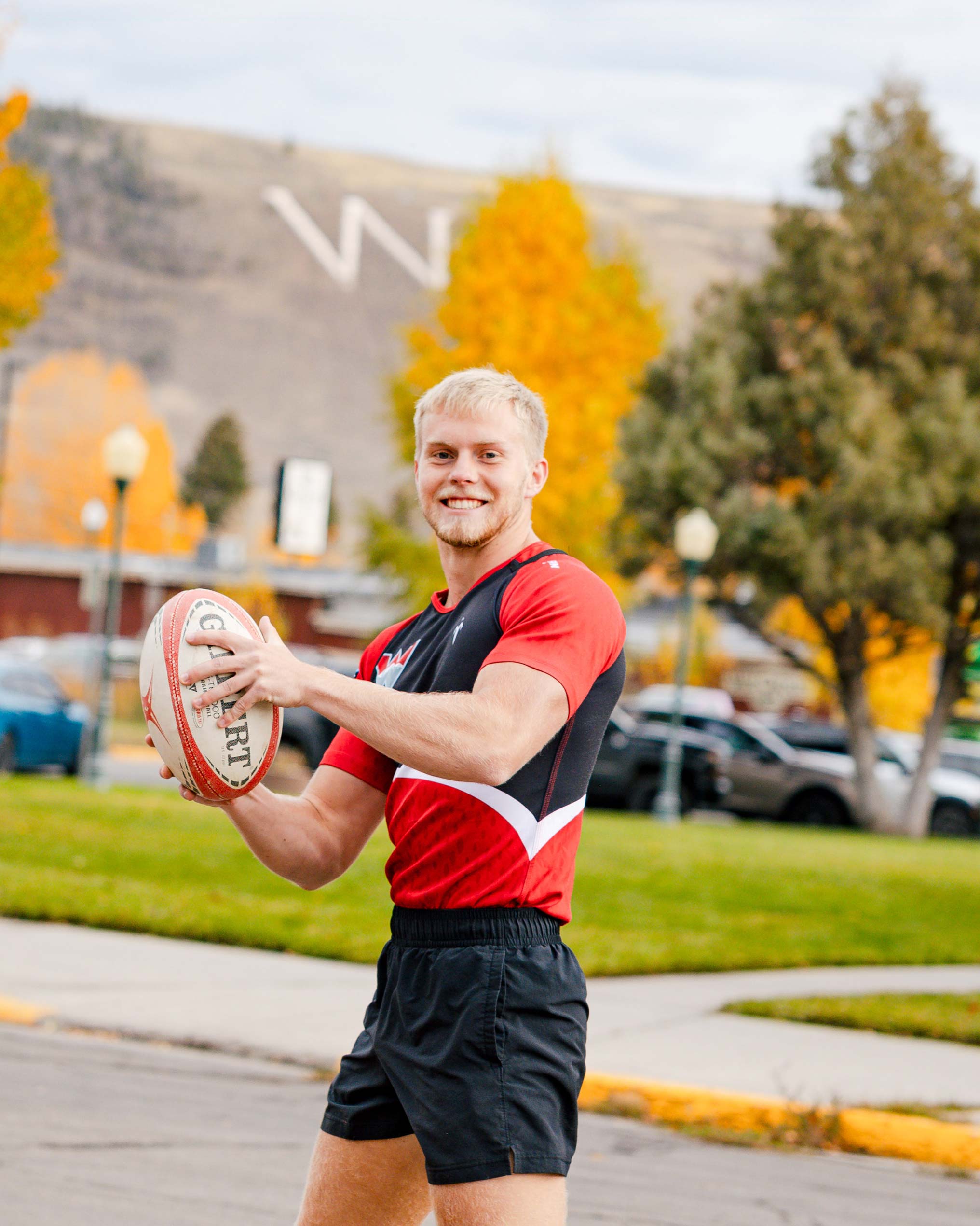 A rugby player holds a rugby ball and smiles with W Mountain behind him during the Homecoming Parade.