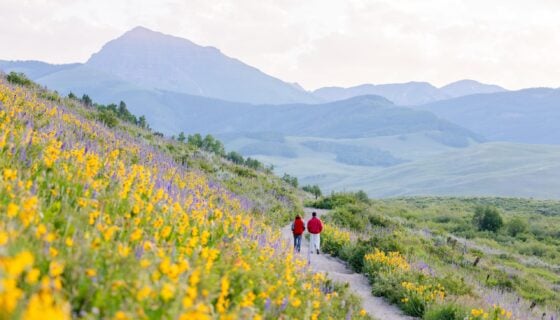Two students wearing red jackets walk the East River Trail at sunrise during wildflower season.