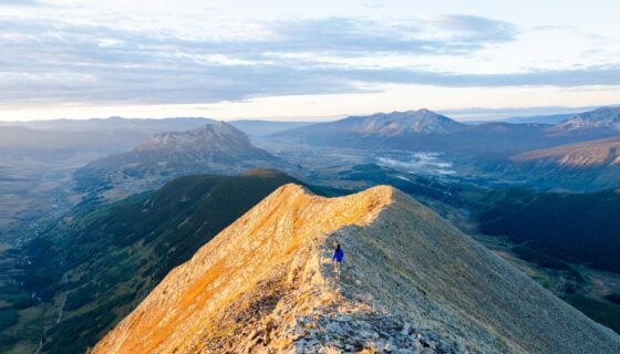 A girl walks down a mountain ridge line at sunrise.