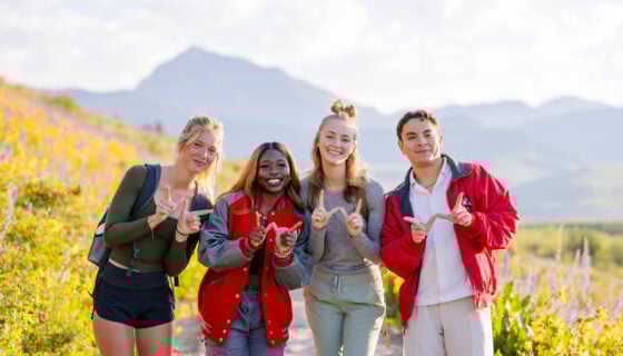 Four students smile in front of Teocalli at sunrise making a W with their hands.