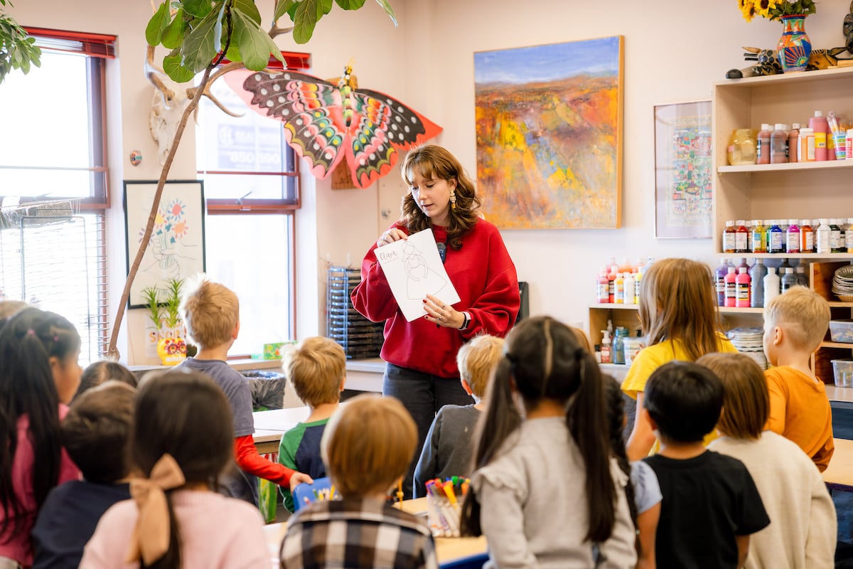 A student teacher holds up a coloring sheet in front of the first grade art class.