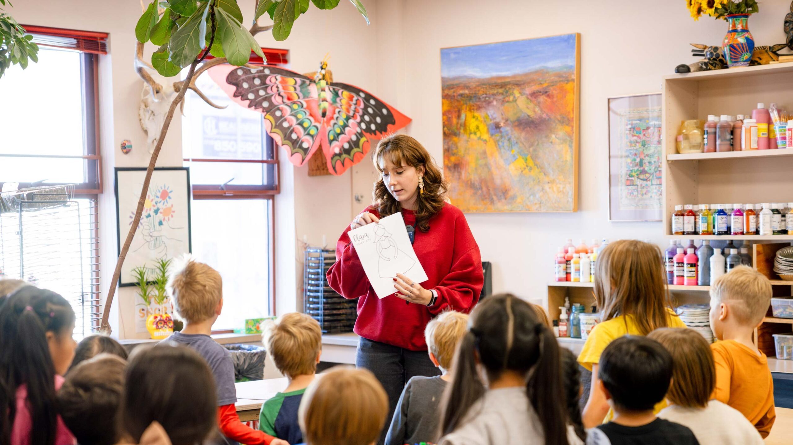 A student teacher holds up a coloring sheet in front of the first grade art class.