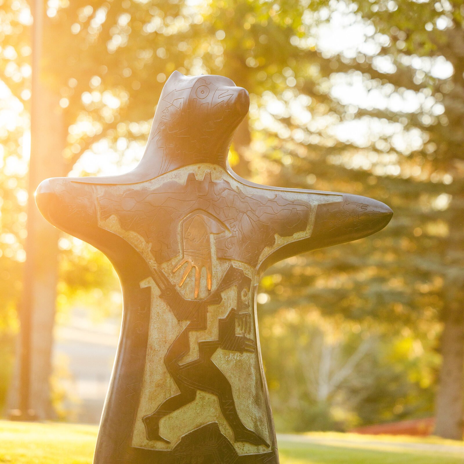 A close up of the Pathfinder Bear statue with morning rays glowing behind it.