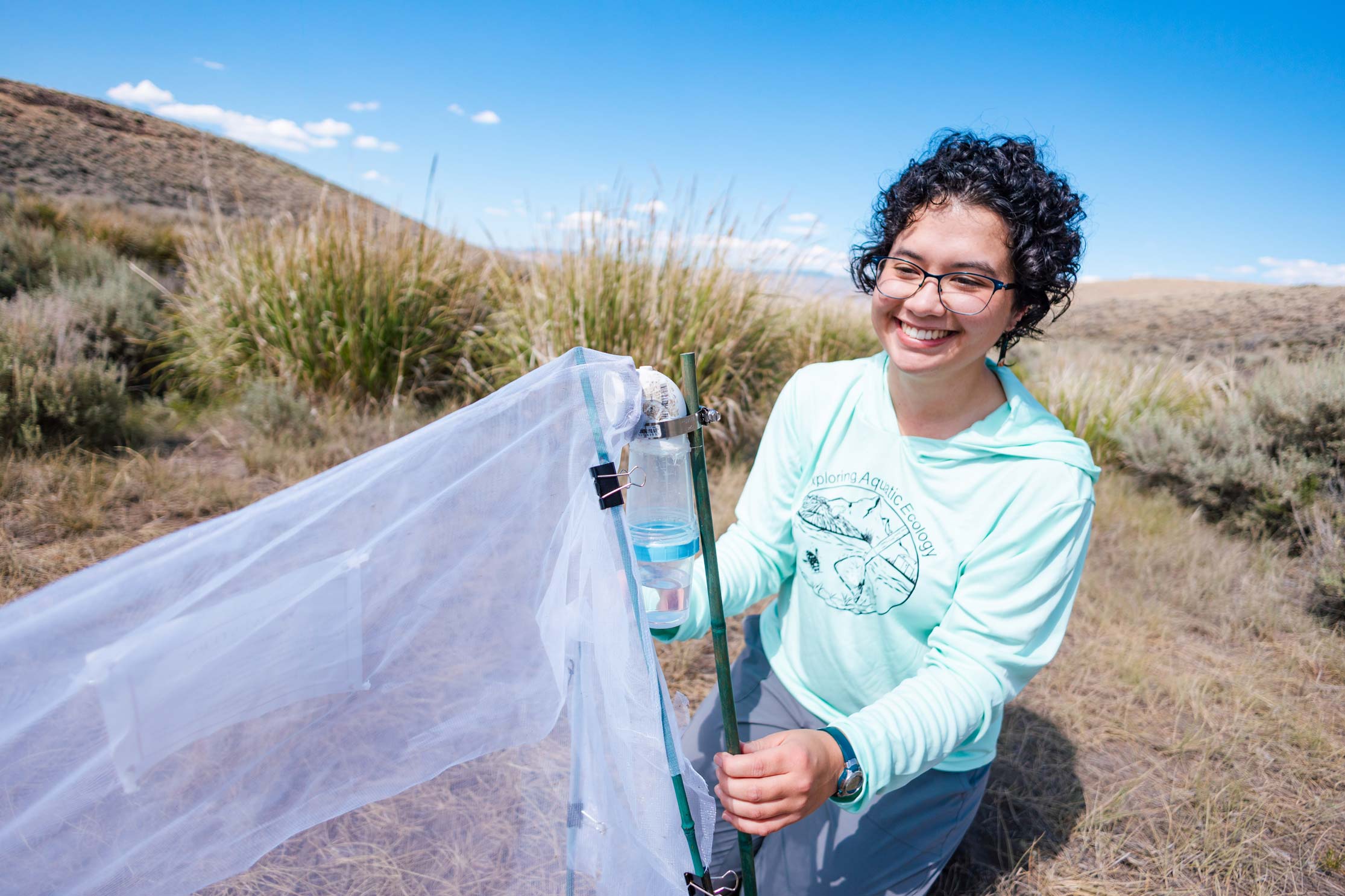 A student smiles as she sets up a bug net to collect data on insect populations in a wet meadow restoration area.
