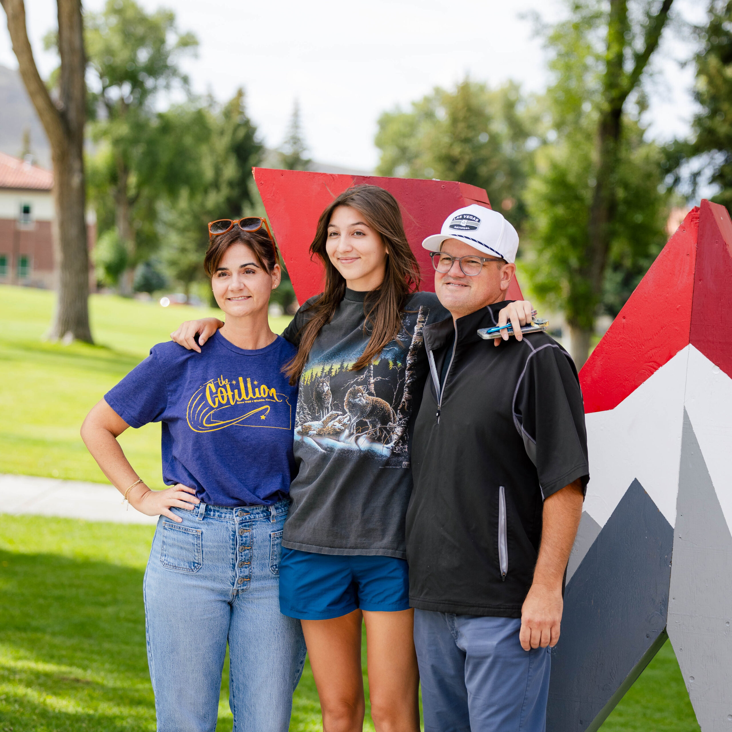 A first-year student stands next to her parents in front of the Western logo for a group picture.