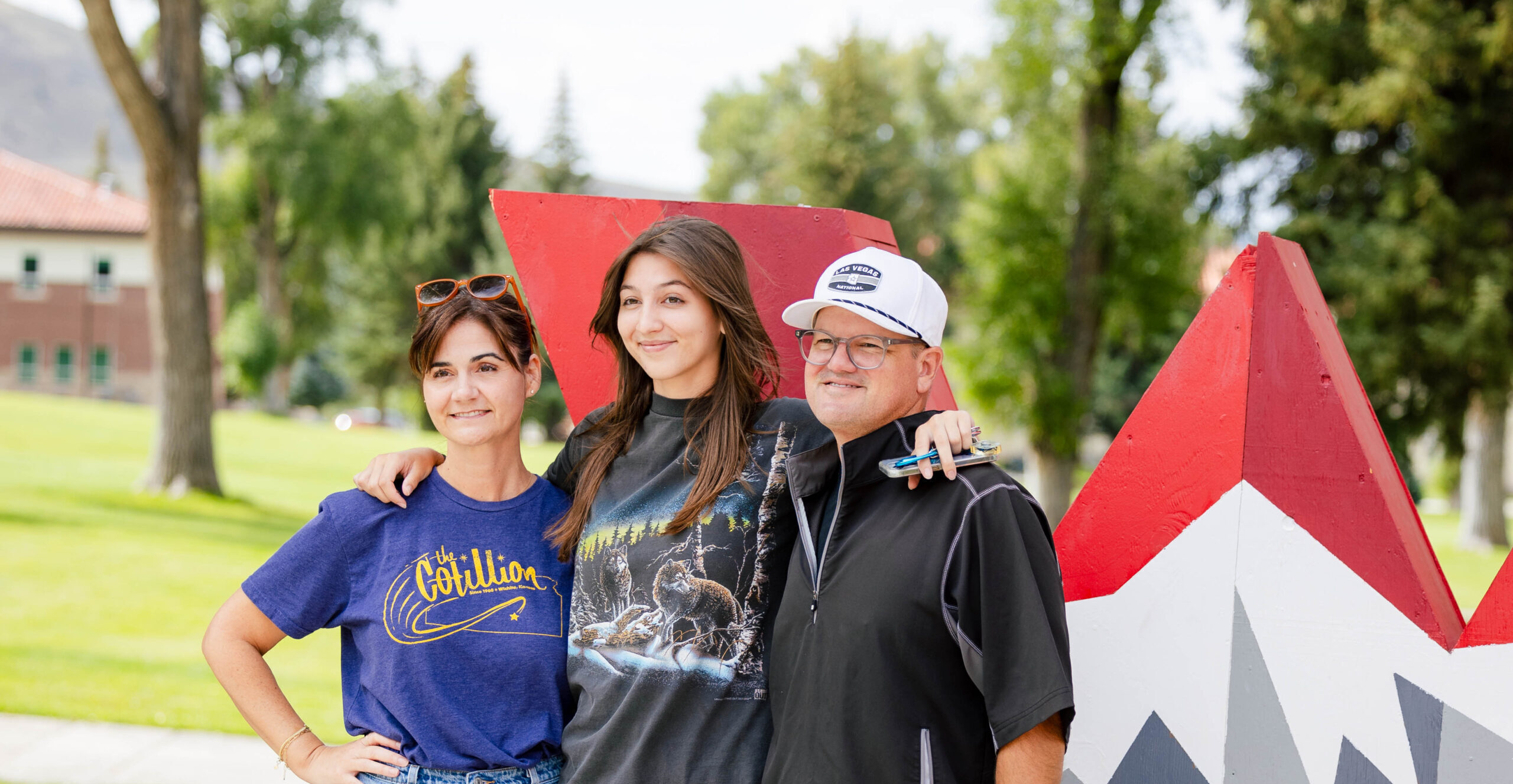 A first-year student stands next to her parents in front of the Western logo for a group picture.