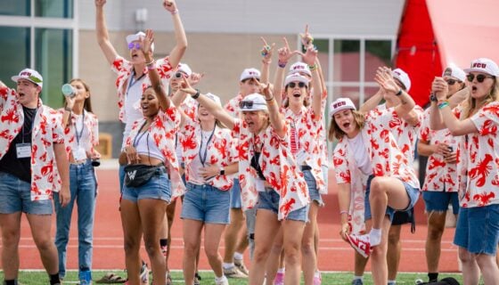 Orientation leaders cheer and raise their arms as they stand on the football field.