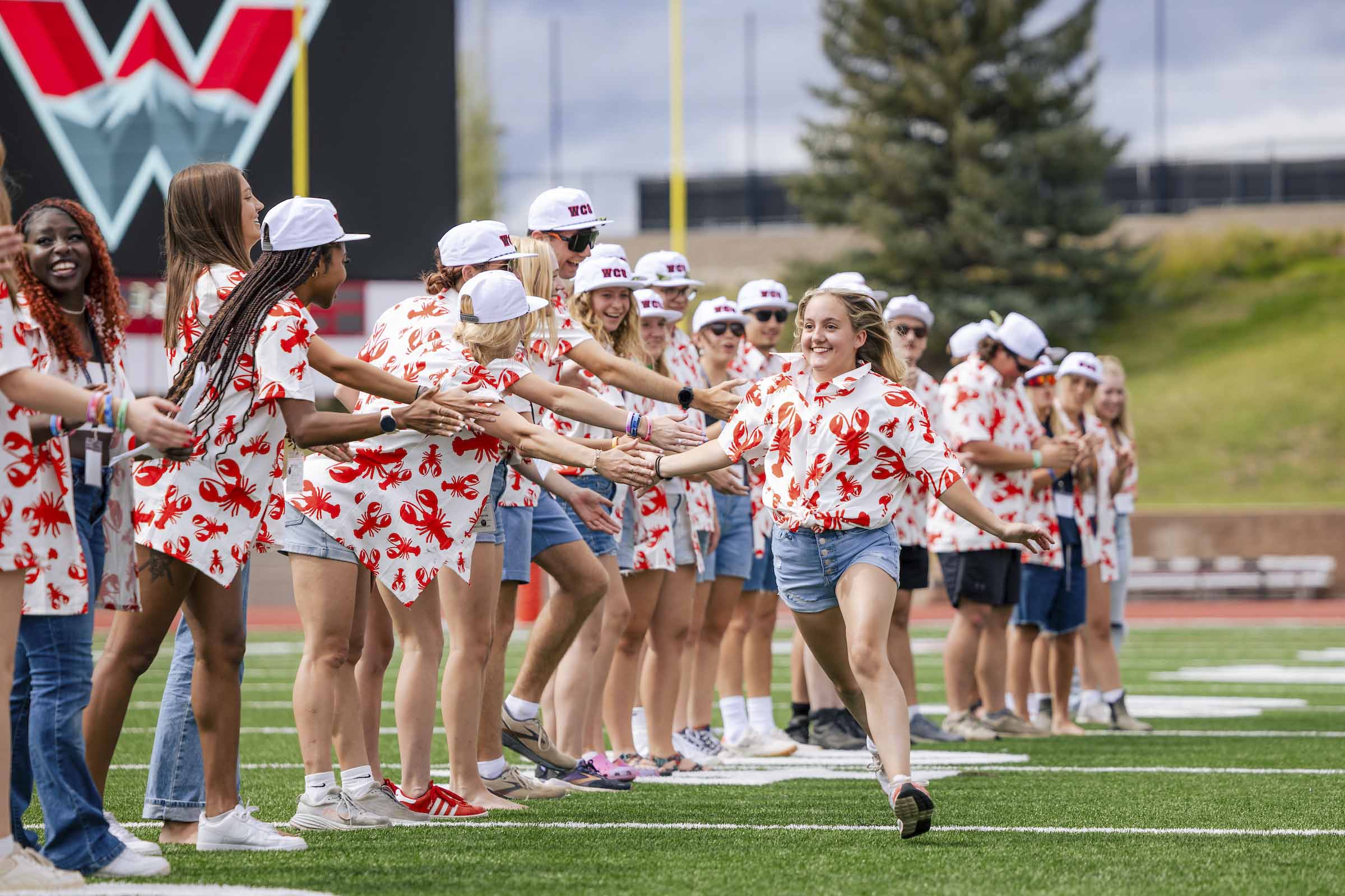 Orientation leaders run and high five each other down a line on the football field as they are introduced.