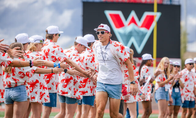 2024 Orientation leaders run and high five each other down a line on the football field as they are introduced.