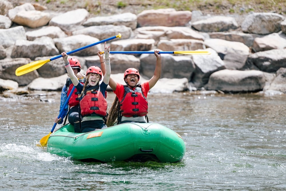 Students hold up their paddles while floating on a raft.