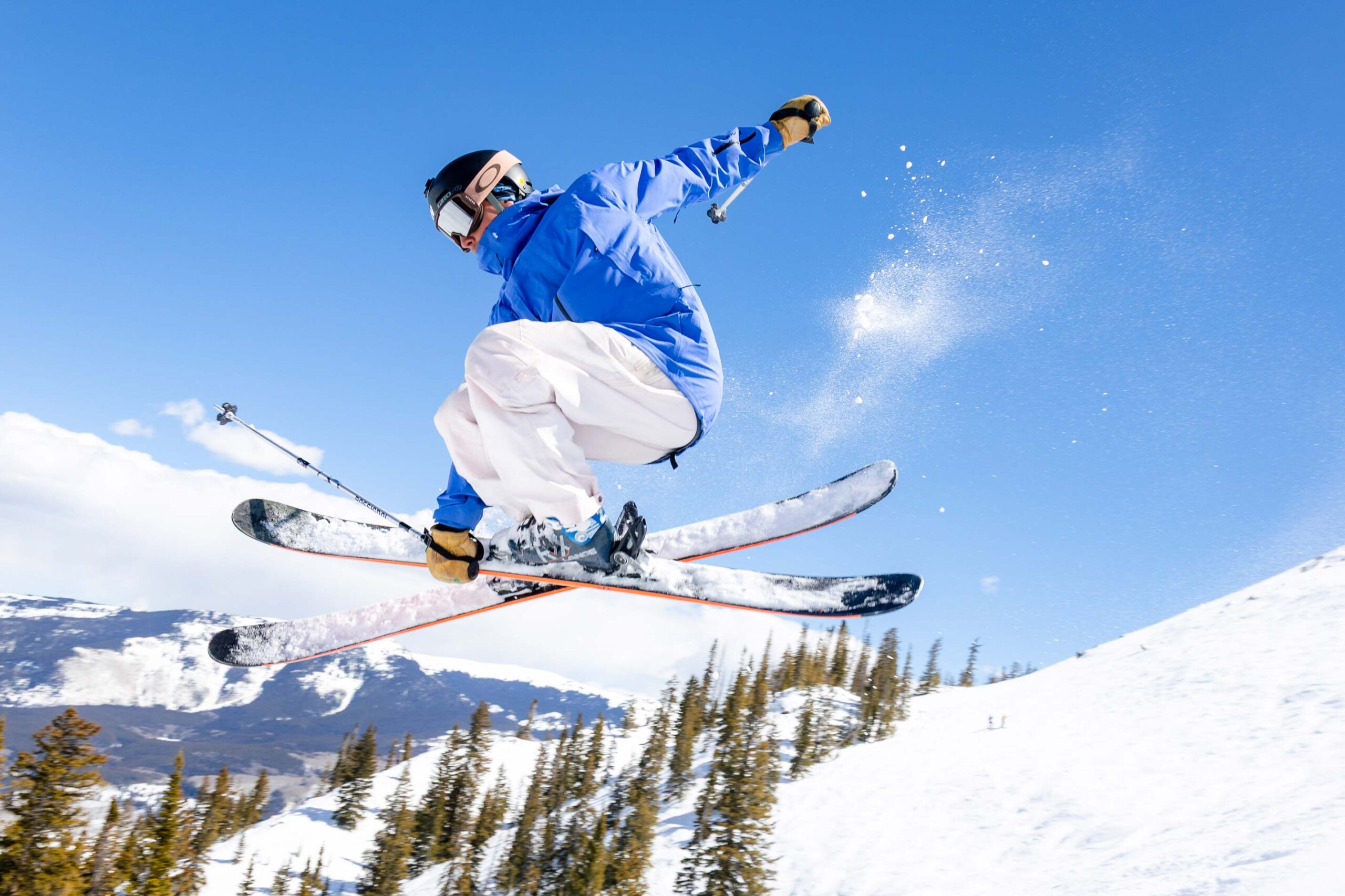 A skier grabs his ski while in the air on a bluebird day.