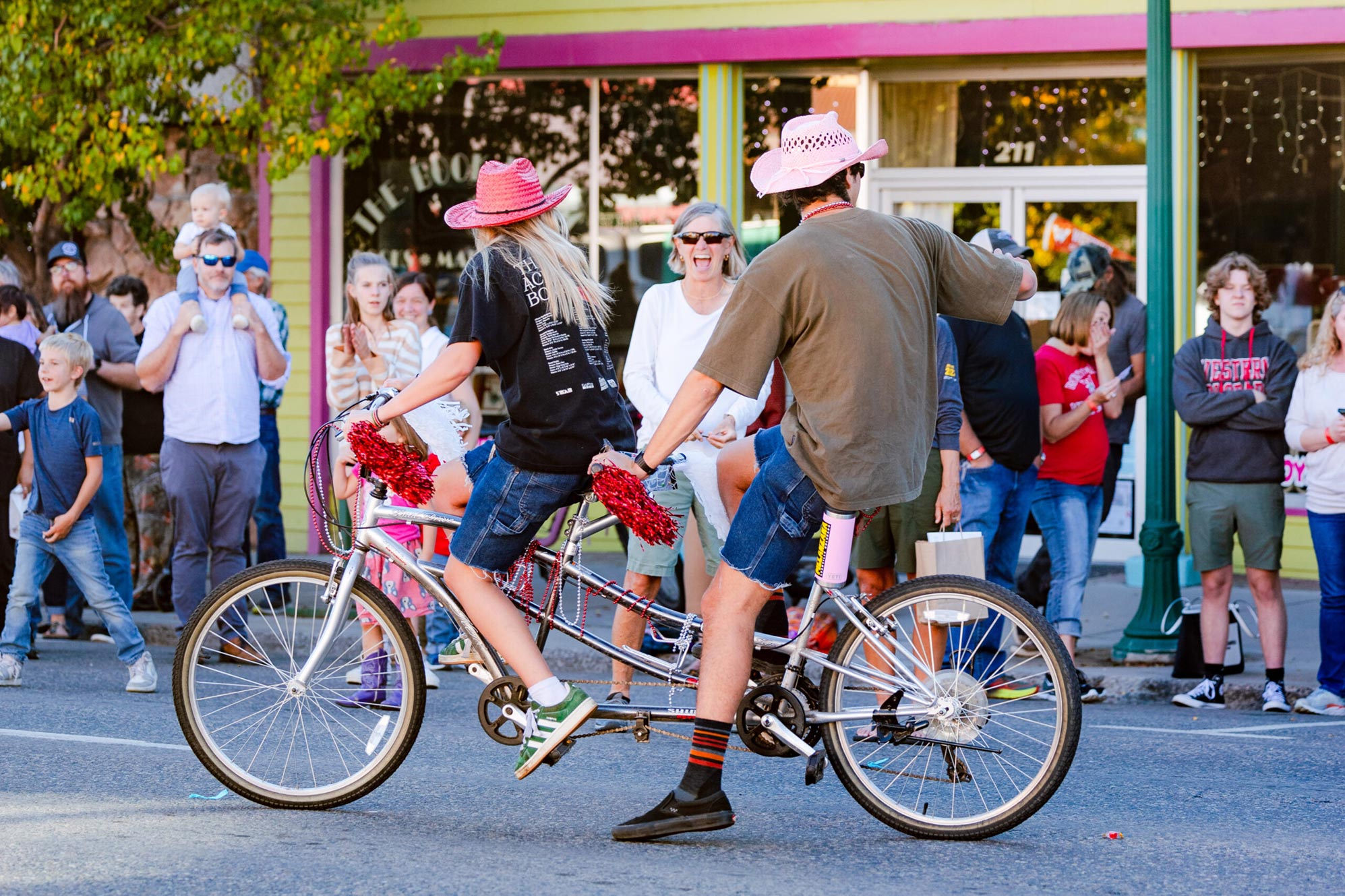 Two students wearing pink cowboy hats ride a tandem townie bike down main street and bring joy to community members during the Homecoming parade.
