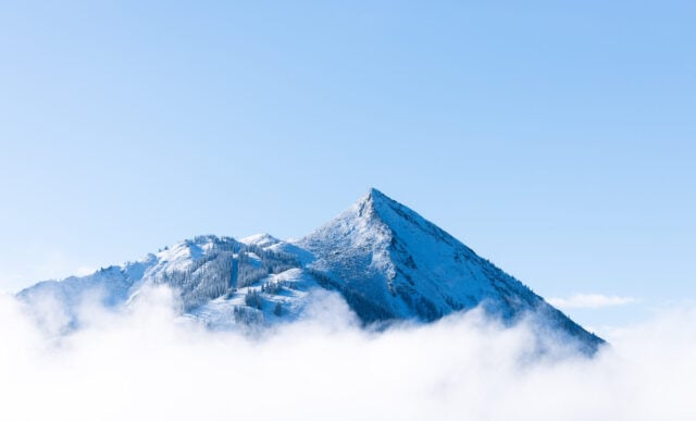 Mount Crested Butte peeks through a layer of clouds on a bluebird day.
