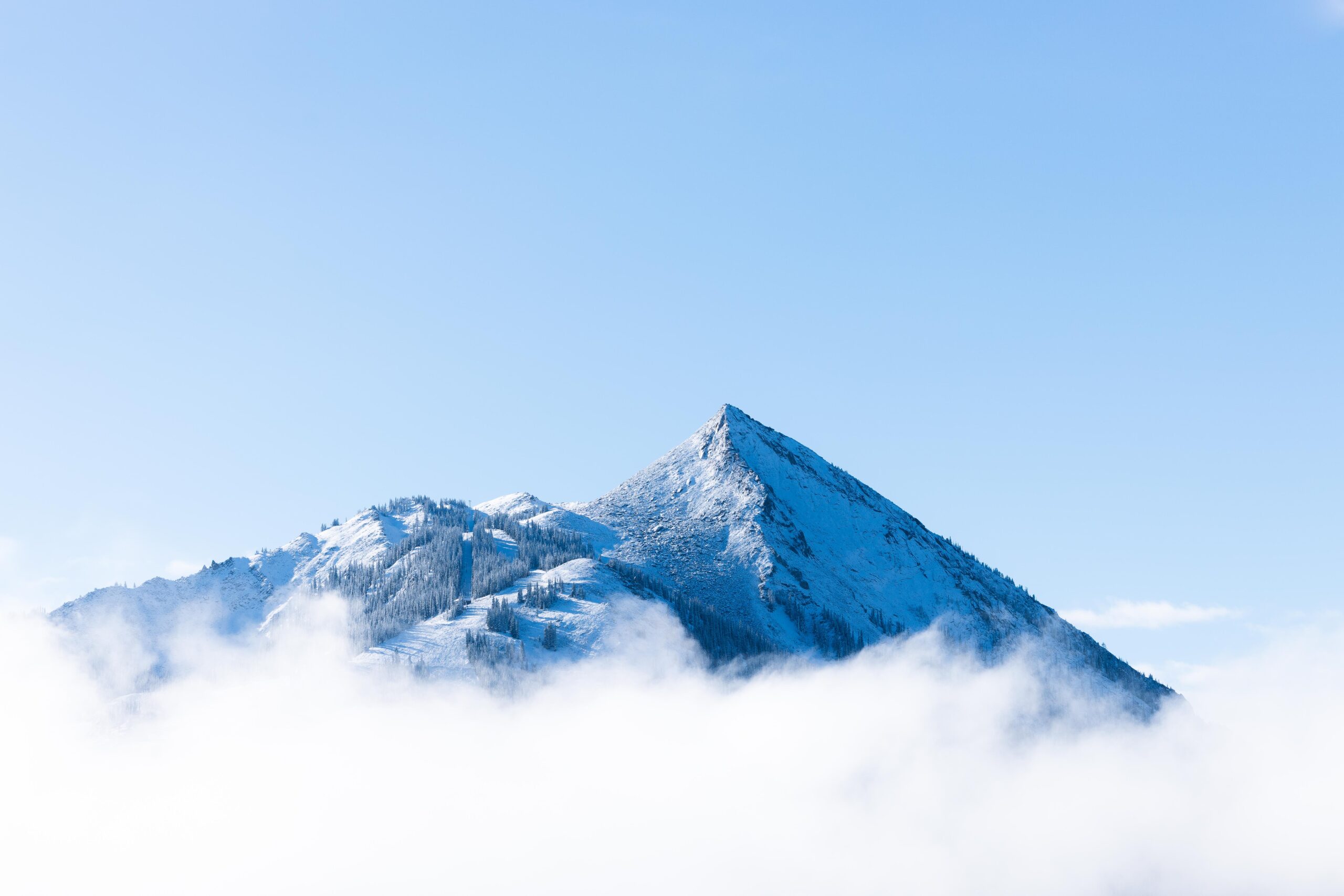 Mt. Crested Butte peeks through a low layer of clouds in a blue sky day.