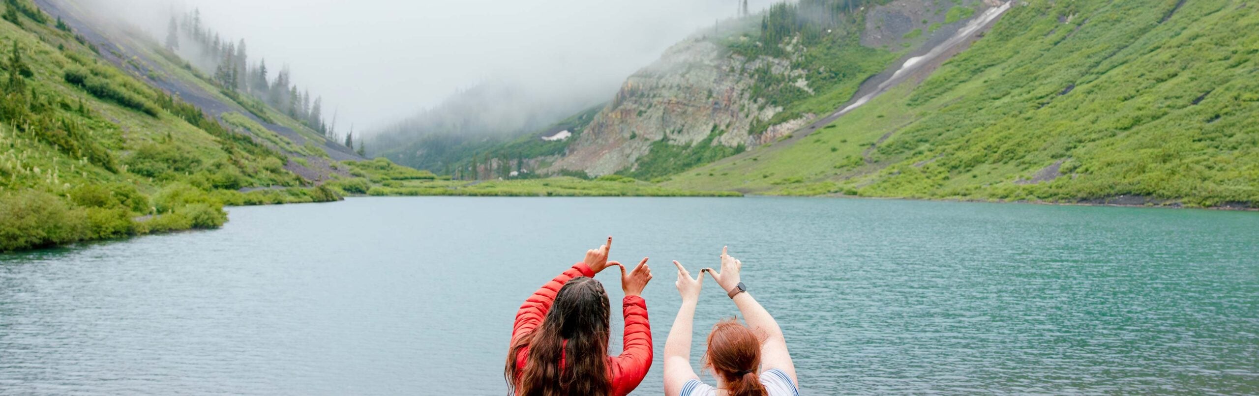 Two girls form a W with their fingers with a foggy lake in the background.