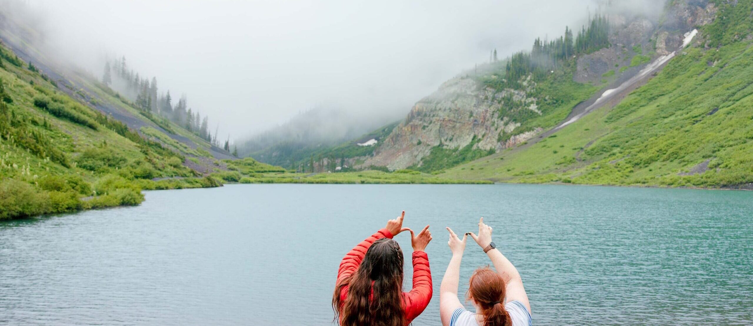 Two students hold up the "W" above their heads in front of Emerald Lake.