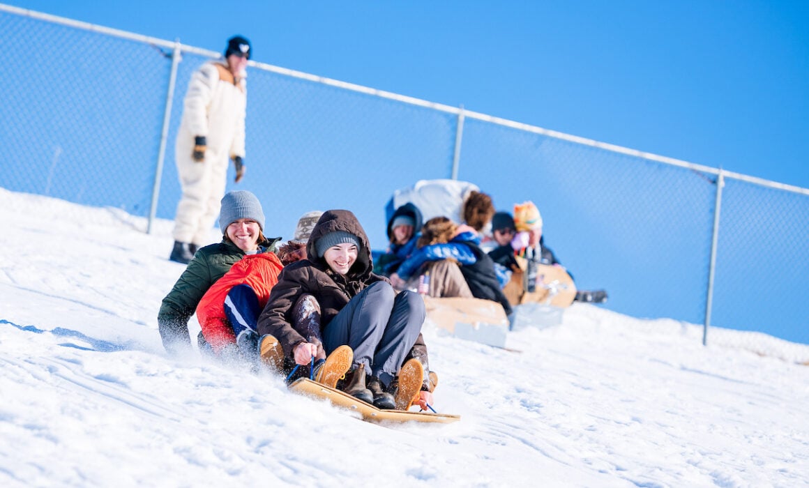 2024 Students race down the Green Monster sledding hill on sleds they made out of cardboard.