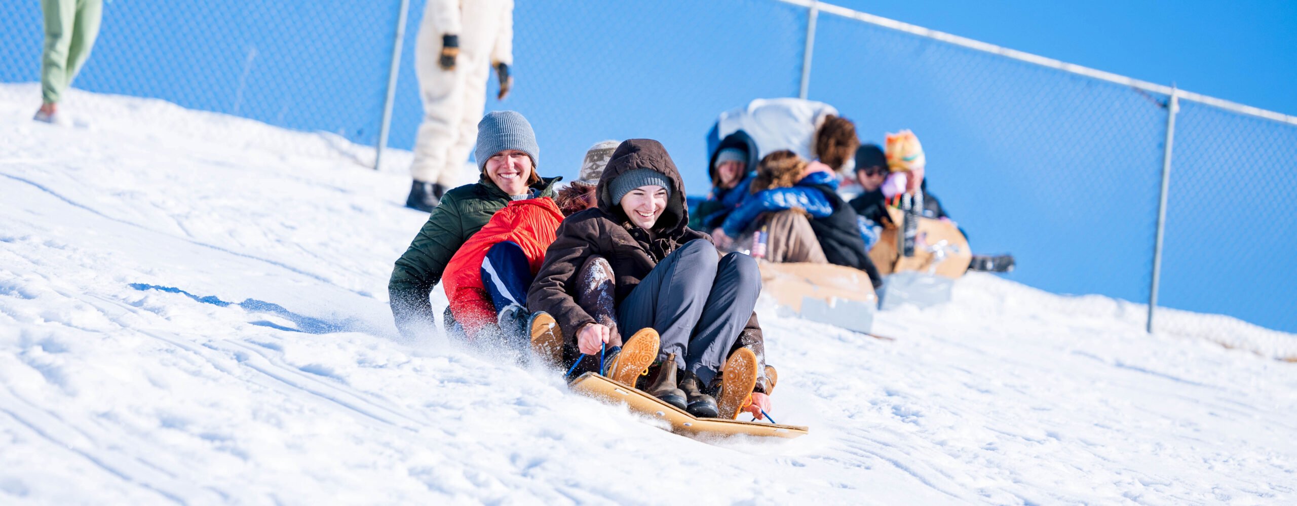 Students race down the Green Monster sledding hill on sleds they made out of cardboard.