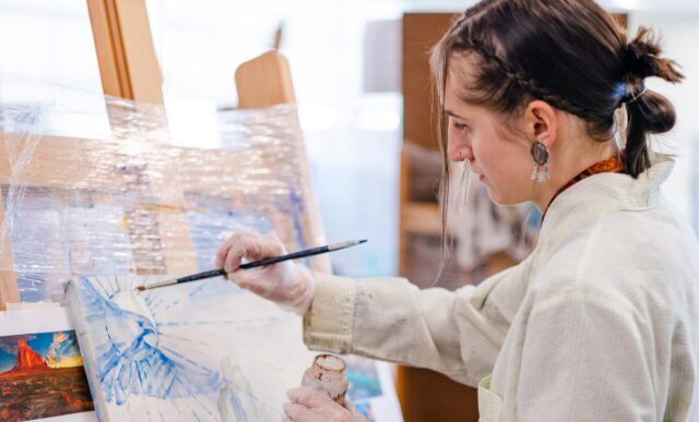 A student stands while working on her vibrant oil painting.