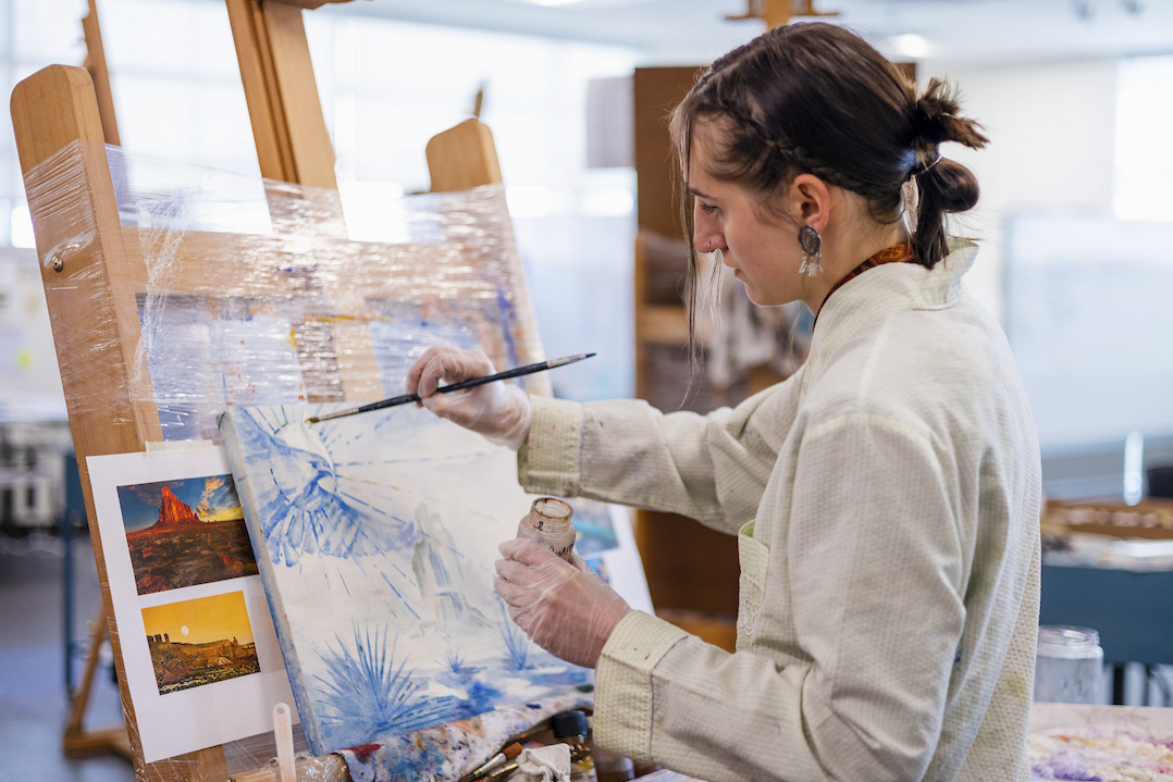 A student stands while working on her vibrant oil painting.
