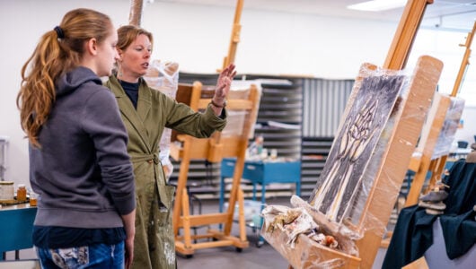 A professor gives feedback to her student next to her on her painting